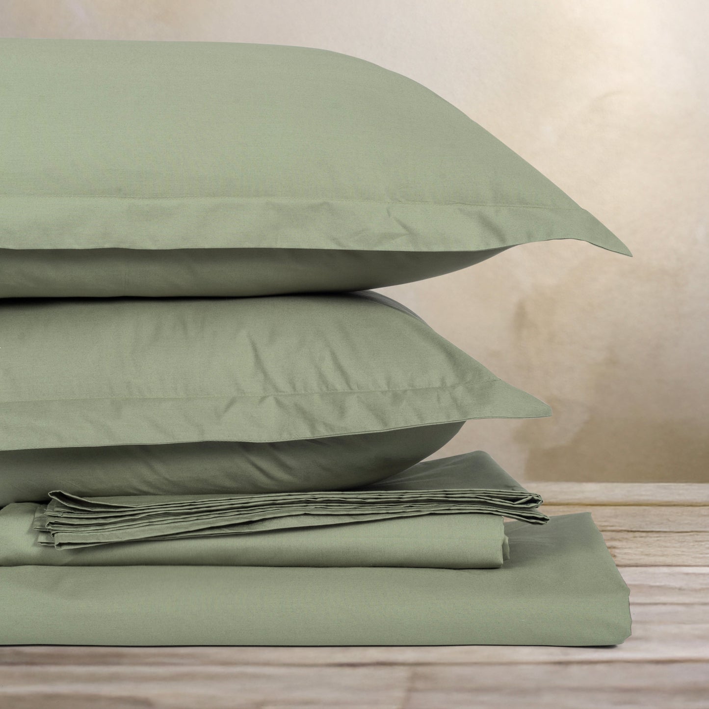 Green bed sheets and pillows stacked on a wooden surface with a neutral background