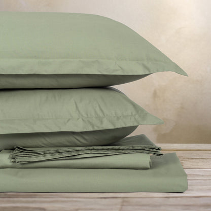 Green bed sheets and pillows stacked on a wooden surface with a neutral background